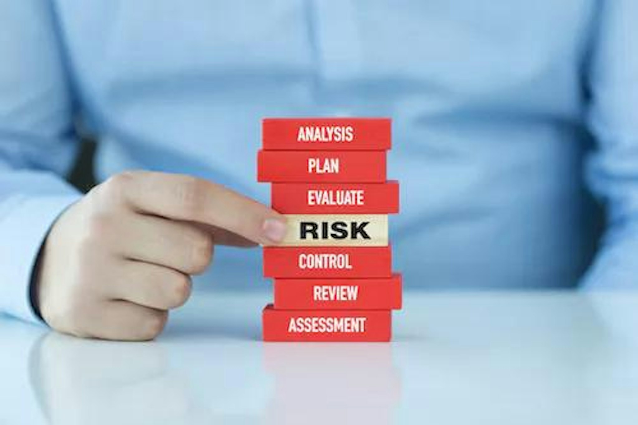 red jenga blocks with white text reading: Analysis, plan, control, renew, refreshment. In the middle of these bricks is a beige block with bold black writing reading "risk" and someone reaching to select this risk block. This image represents the need for risk management best practices for entity management.