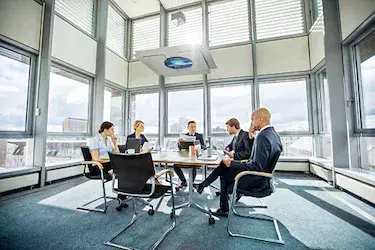 Nonprofit board discusses how they compare to corporates while sitting around a table in a building with lots of windows.