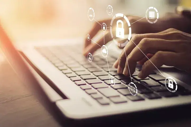 Person typing on laptop with graphic overlay of cybersecurity symbols jointed together like a mind map above keyboard