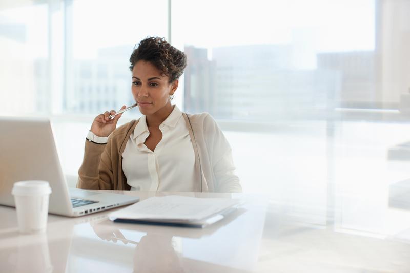 Person holds pen to their chin while reading about corporate governance and entity management on their laptop in light-filled office.