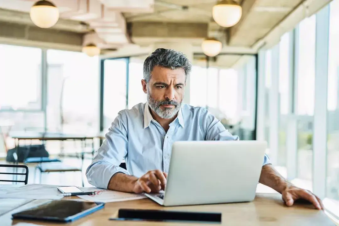 Man sits at a desk in an office, looking at a laptop